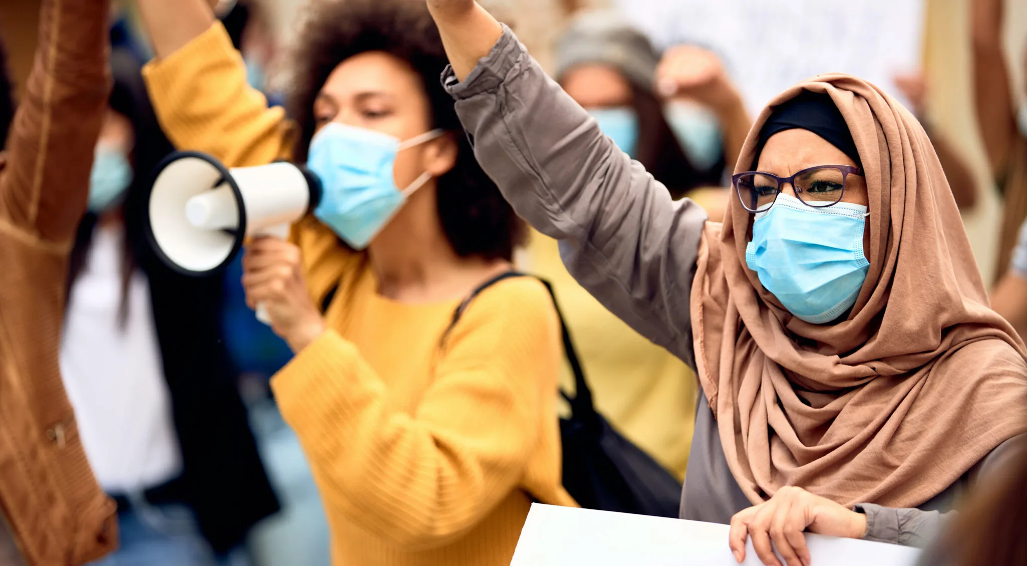 Muslim woman wearing protective face mask and supporting anti-racism movement with group of people on city streets.