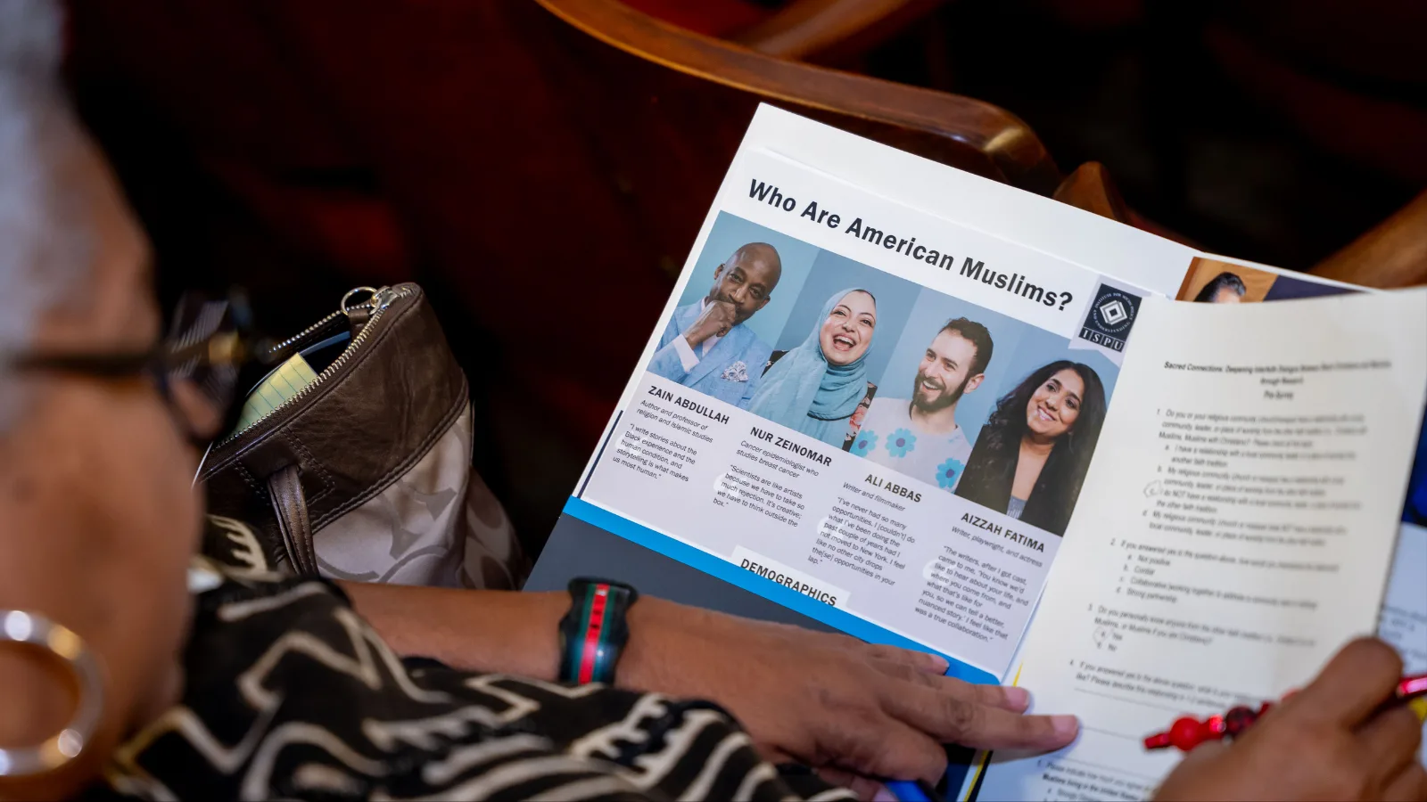 A person holding a booklet open to a page titled “Who Are American Muslims?” featuring photos and brief descriptions of four individuals, with other pamphlets and a pen also visible.